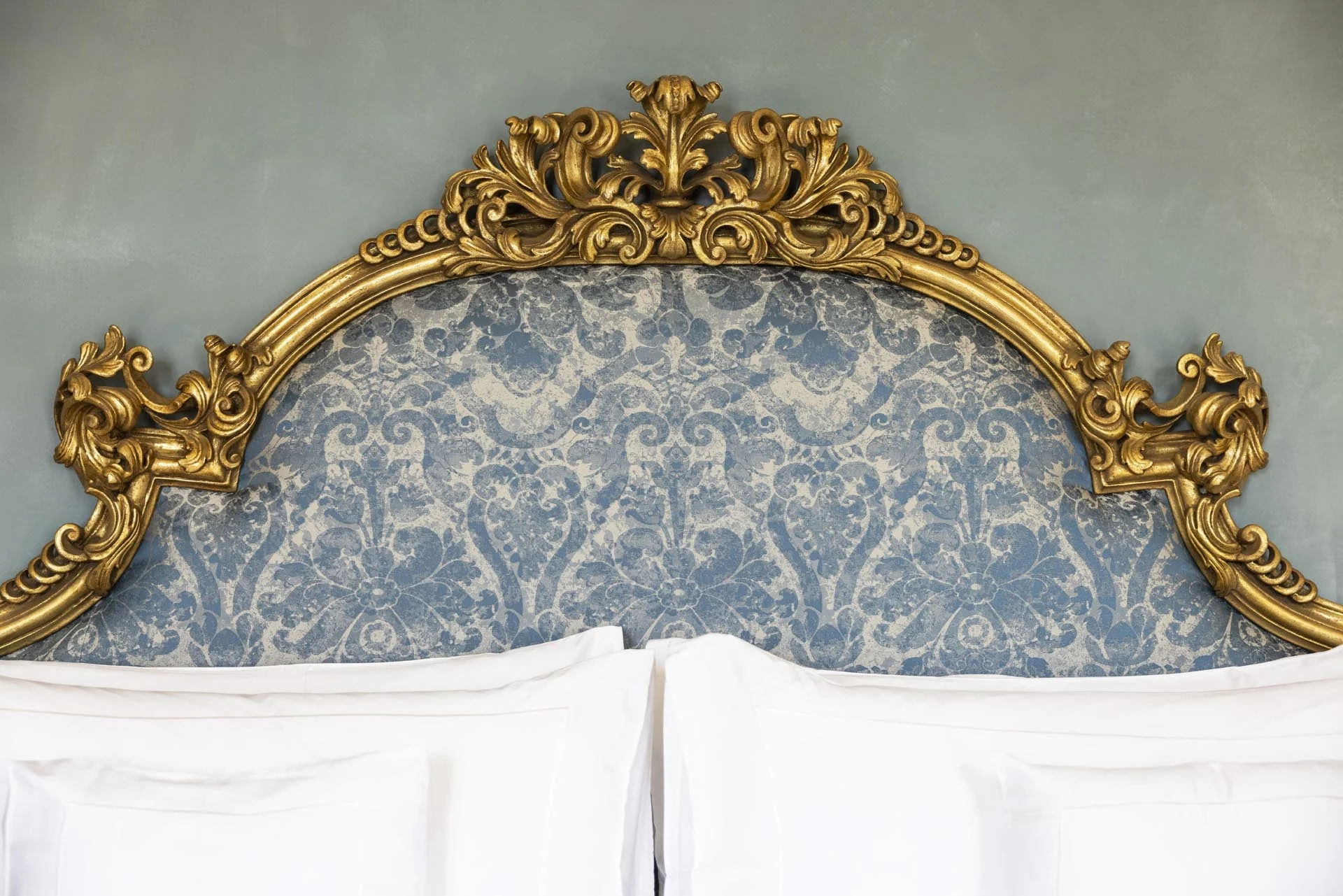 Cama com cabeceira dourada em uma suíte do Passalacqua